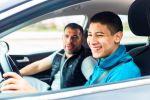 un hijo sonríe mientras maneja un carro con su papa a su lado